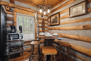 Ein rustikales Blockhaus-Interieur mit einem Holzespeisetisch, gedeckt für vier Personen, einer Kaffeestation und einem gerahmten Bild an der Wand.