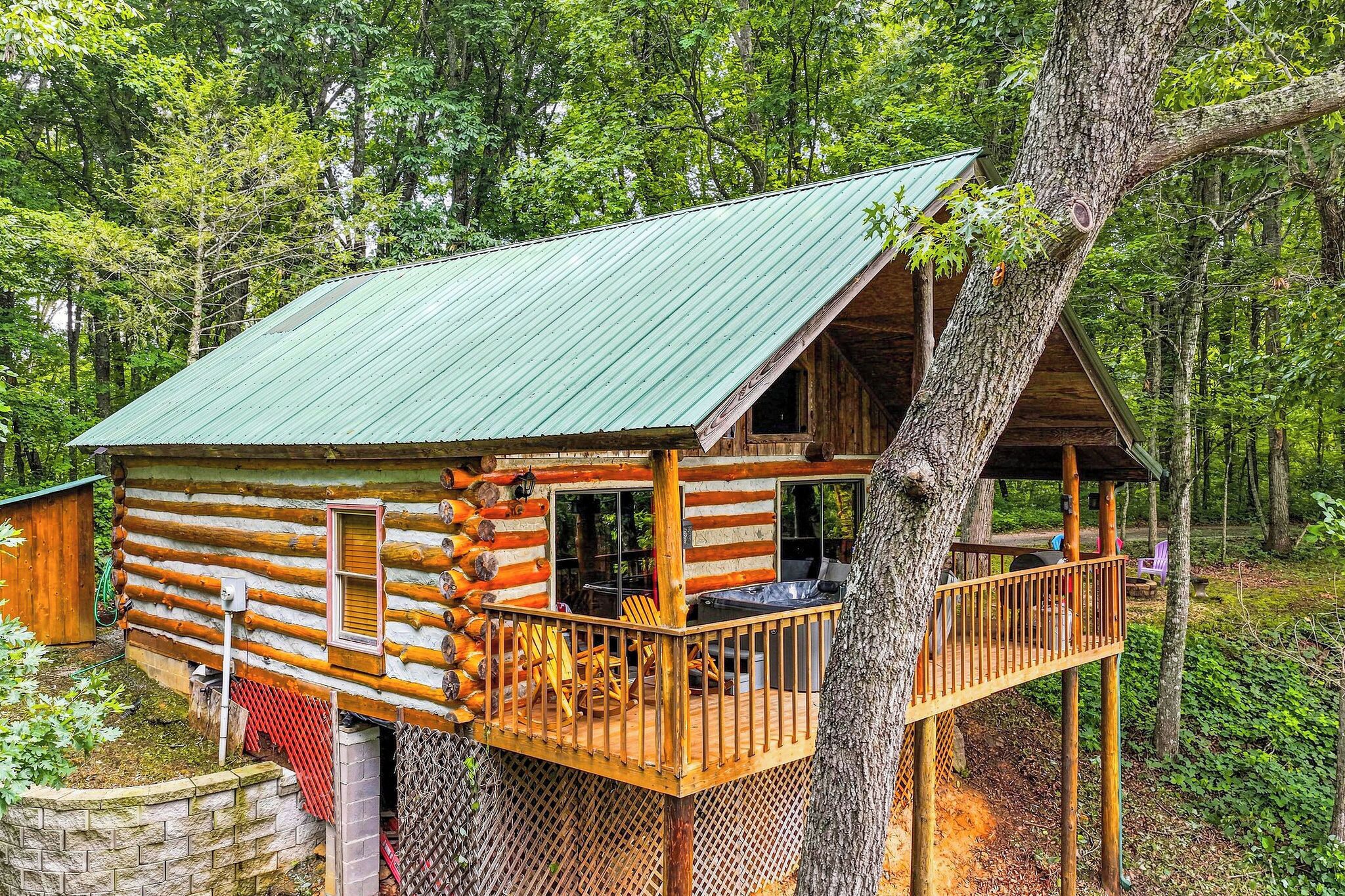 Una cabaña de troncos con techo verde, terraza de madera y un gran tronco de árbol que sostiene la estructura.