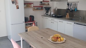 A modern kitchen with white cabinets, a wooden dining table, and a variety of kitchen utensils. - Villa in Couleur 9 -bed (BRINDAS)