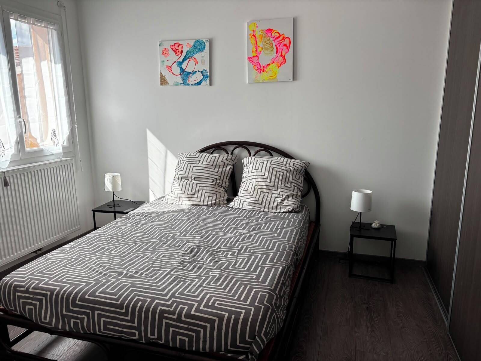 Une chambre à coucher comprenant un lit, deux tables de chevet, une fenêtre et deux œuvres d’art murales.
