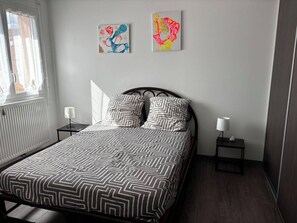 Ein Schlafzimmer mit einem Bett, zwei Nachttischen, einem Fenster und zwei Wandbildern.