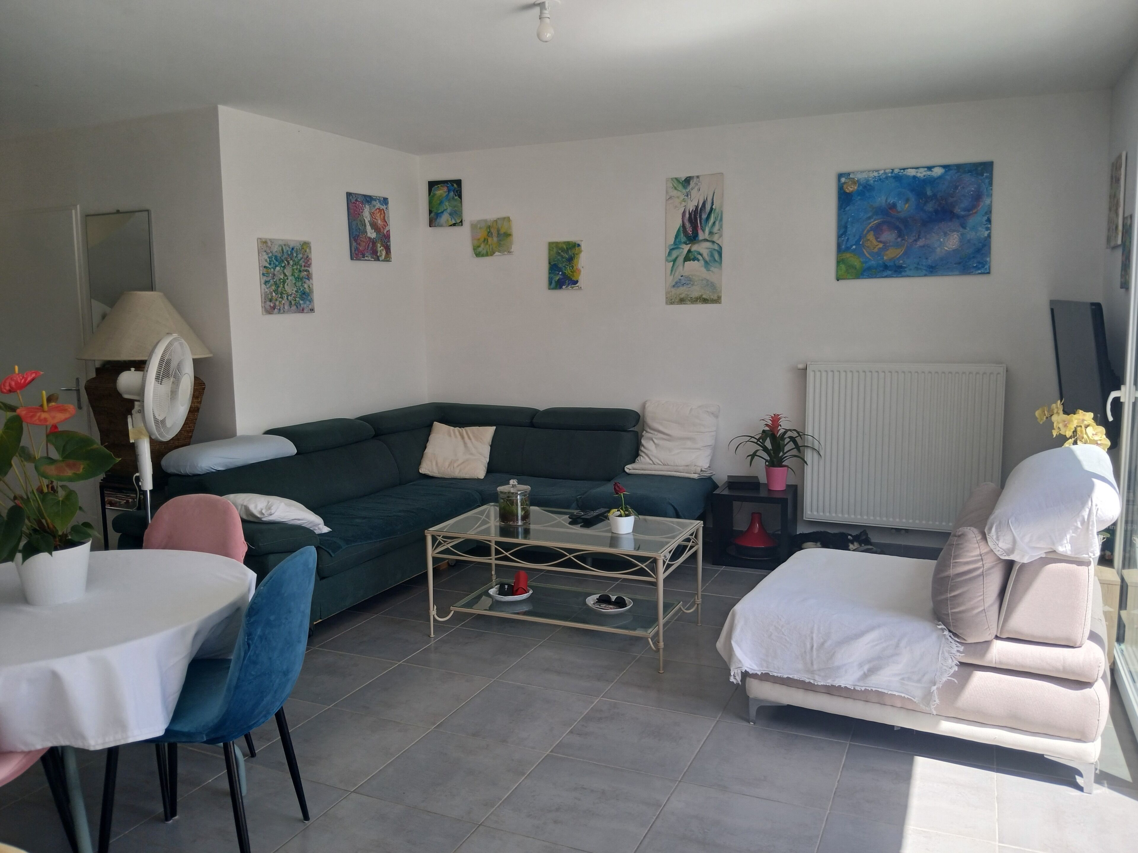Ein Wohnzimmer mit einer Eckcouch, einem Couchtisch, einem Esstisch mit Stühlen und Bildern an den Wänden.