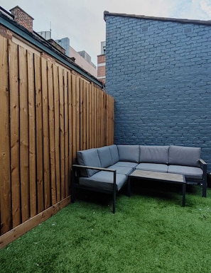 A wooden fence, a blue brick wall, and a gray sectional sofa on a grassy lawn. - Unique 4BR City Apartment | Terrace + Sleeps 10 (Liverpool)