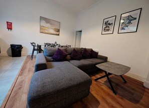 A modern living room with a sectional sofa, a small table, and two framed artworks on the wall. - Unique 4BR City Apartment | Terrace + Sleeps 10 (Liverpool)