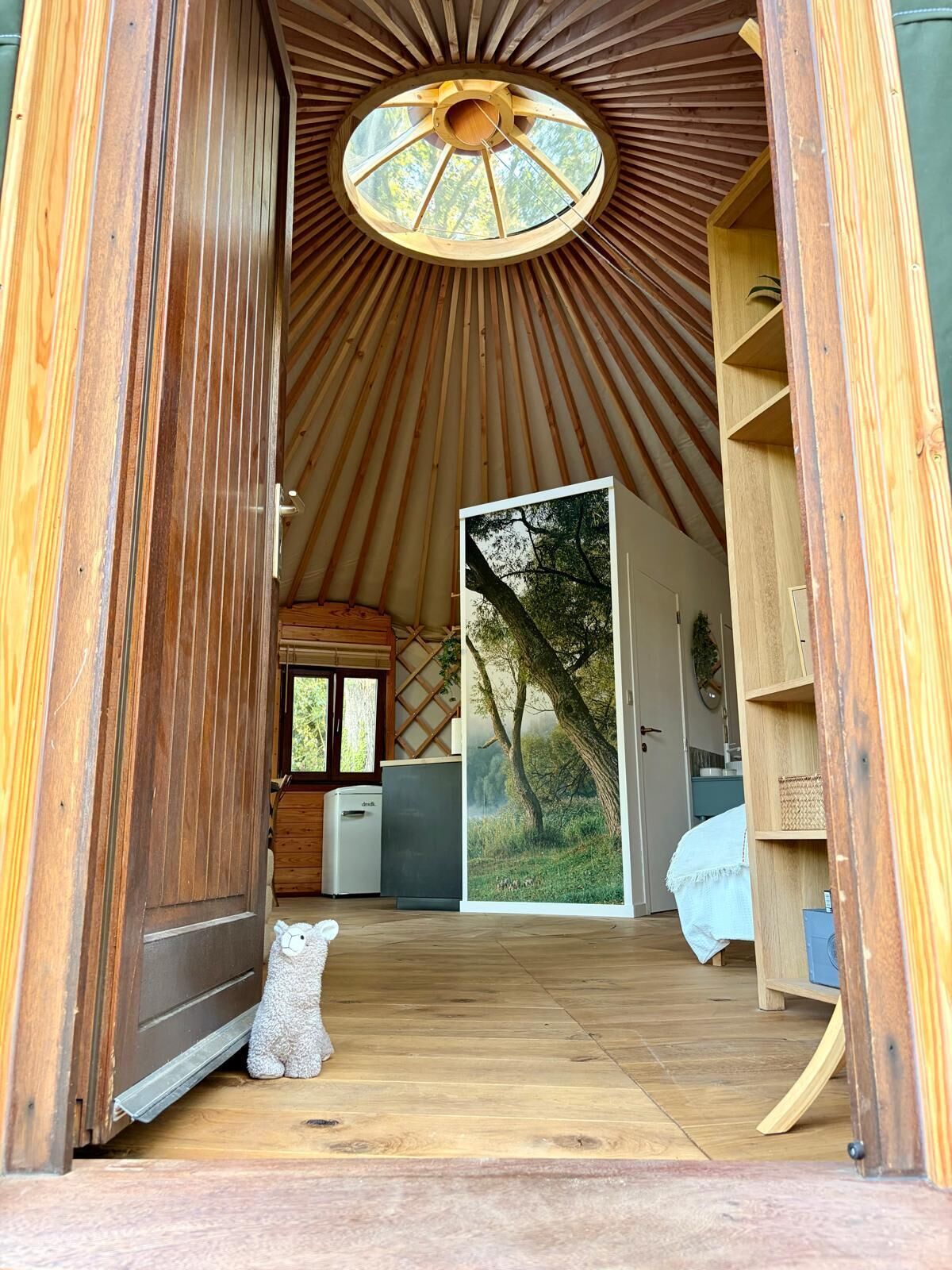 A wooden interior with a circular skylight, a white bear sculpture, and a large window with a forest scene.