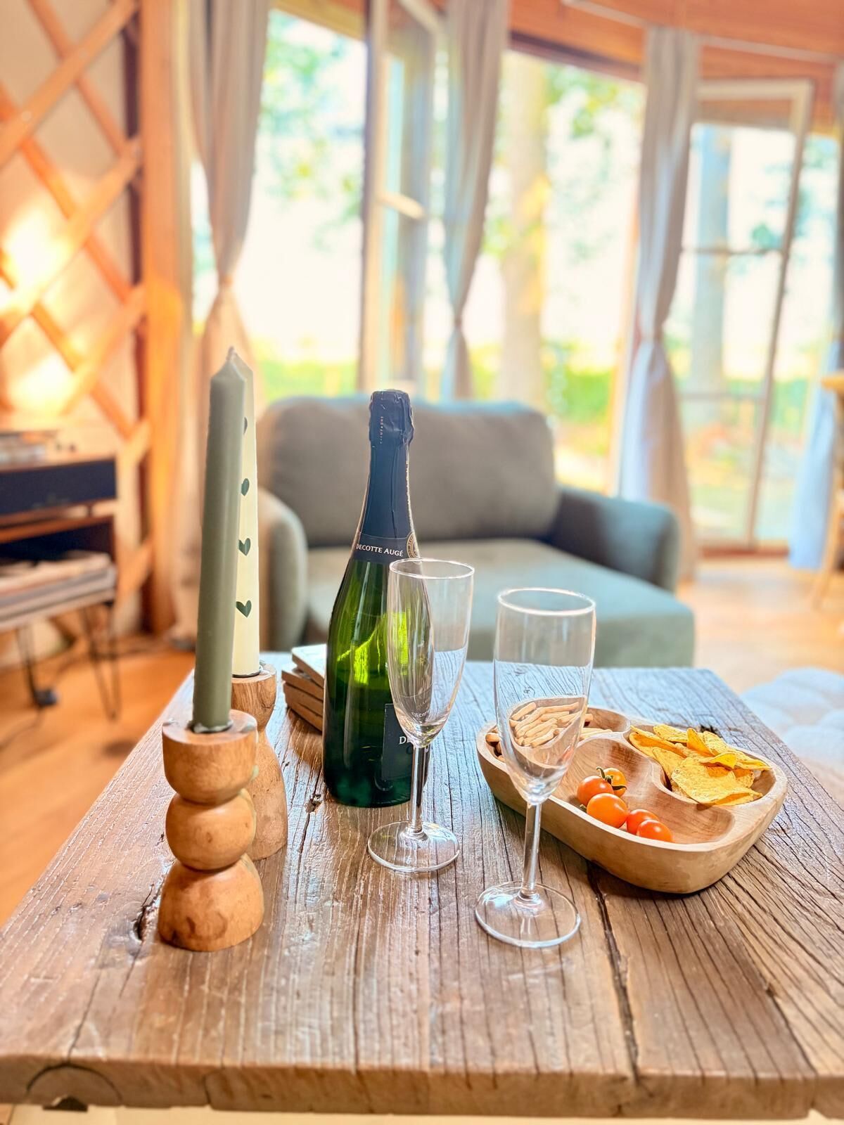 Ett träbord med en flaska champagne, två glas och ett träbricka med tilltugg.