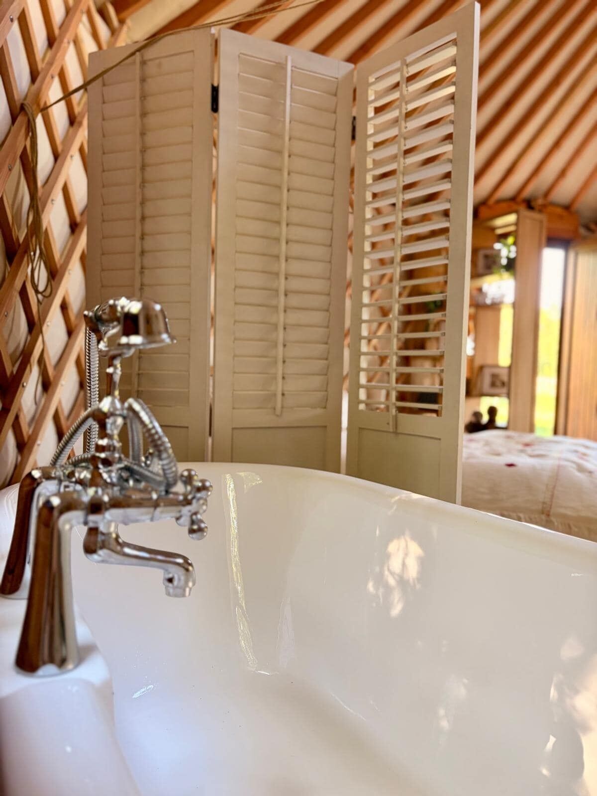 Une salle de bain avec une baignoire, un mur décoré d’un treillis en bois et un lit en arrière-plan.