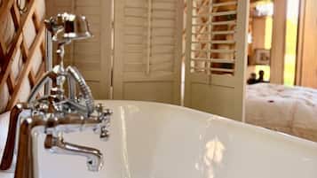 Une salle de bain avec une baignoire, un mur décoré d’un treillis en bois et un lit en arrière-plan.