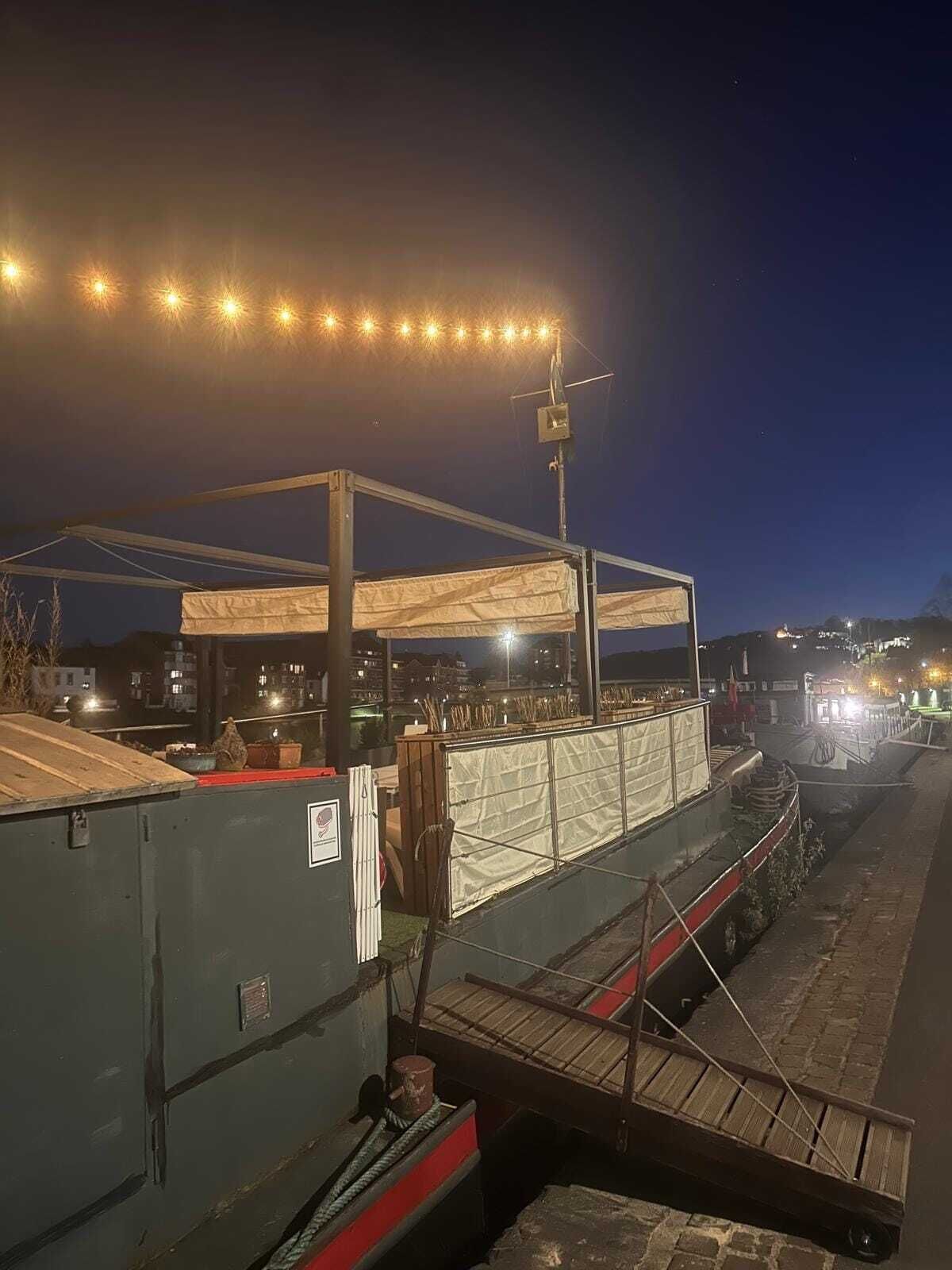 Zona costera con una estructura cubierta, posiblemente un restaurante o bar, y un muelle con un barco.