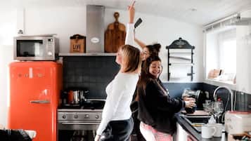 Il y a une cuisine avec un réfrigérateur rouge, un four à micro-ondes et une cuisinière. Deux personnes se trouvent dans la cuisine.
