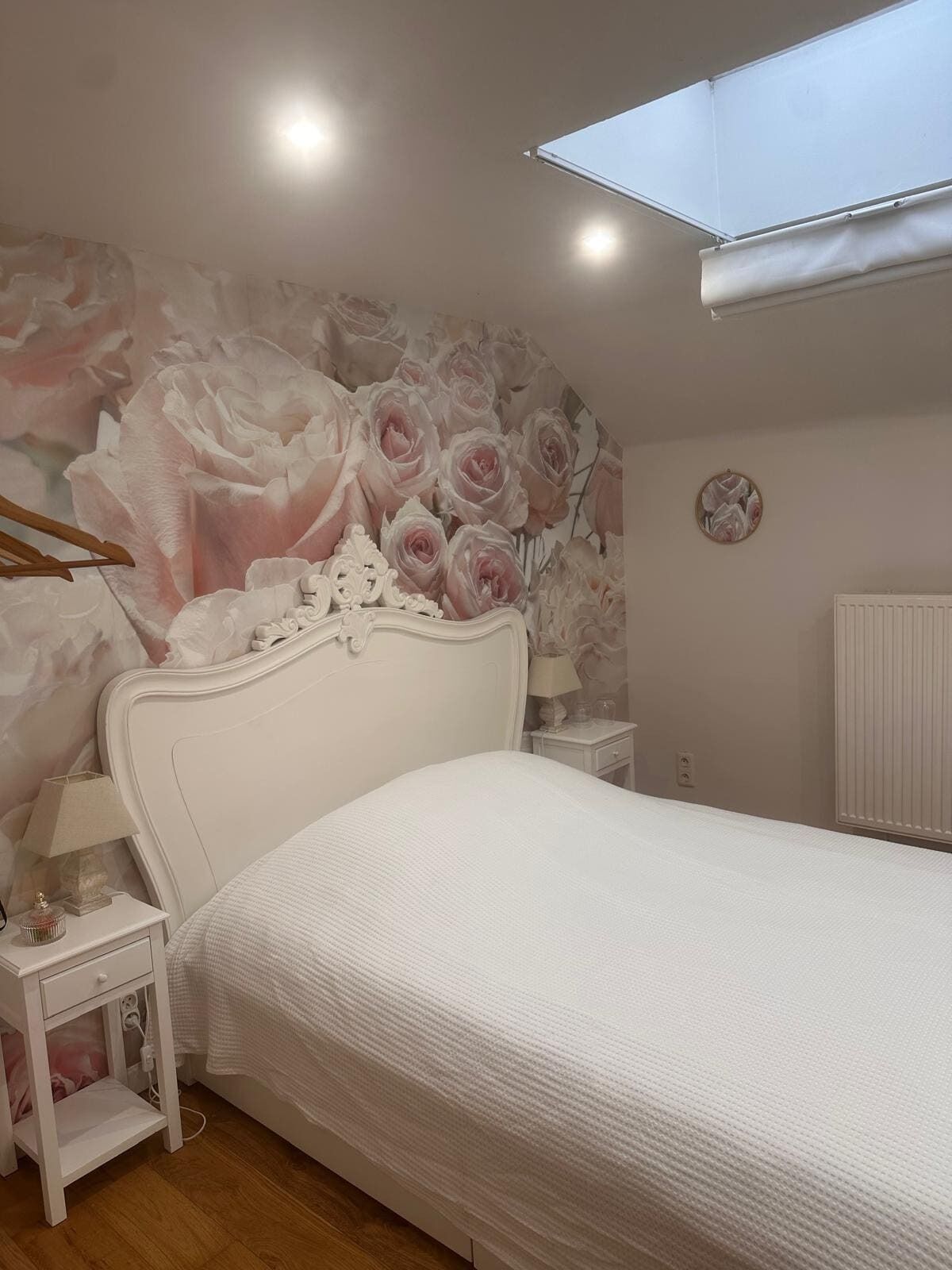Een slaapkamer met een bed, nachtkastje, lamp, radiator en dakraam.