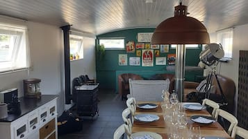 Een eethoek met een lange tafel gedekt voor een maaltijd, een koffieapparaat en een koelkast.