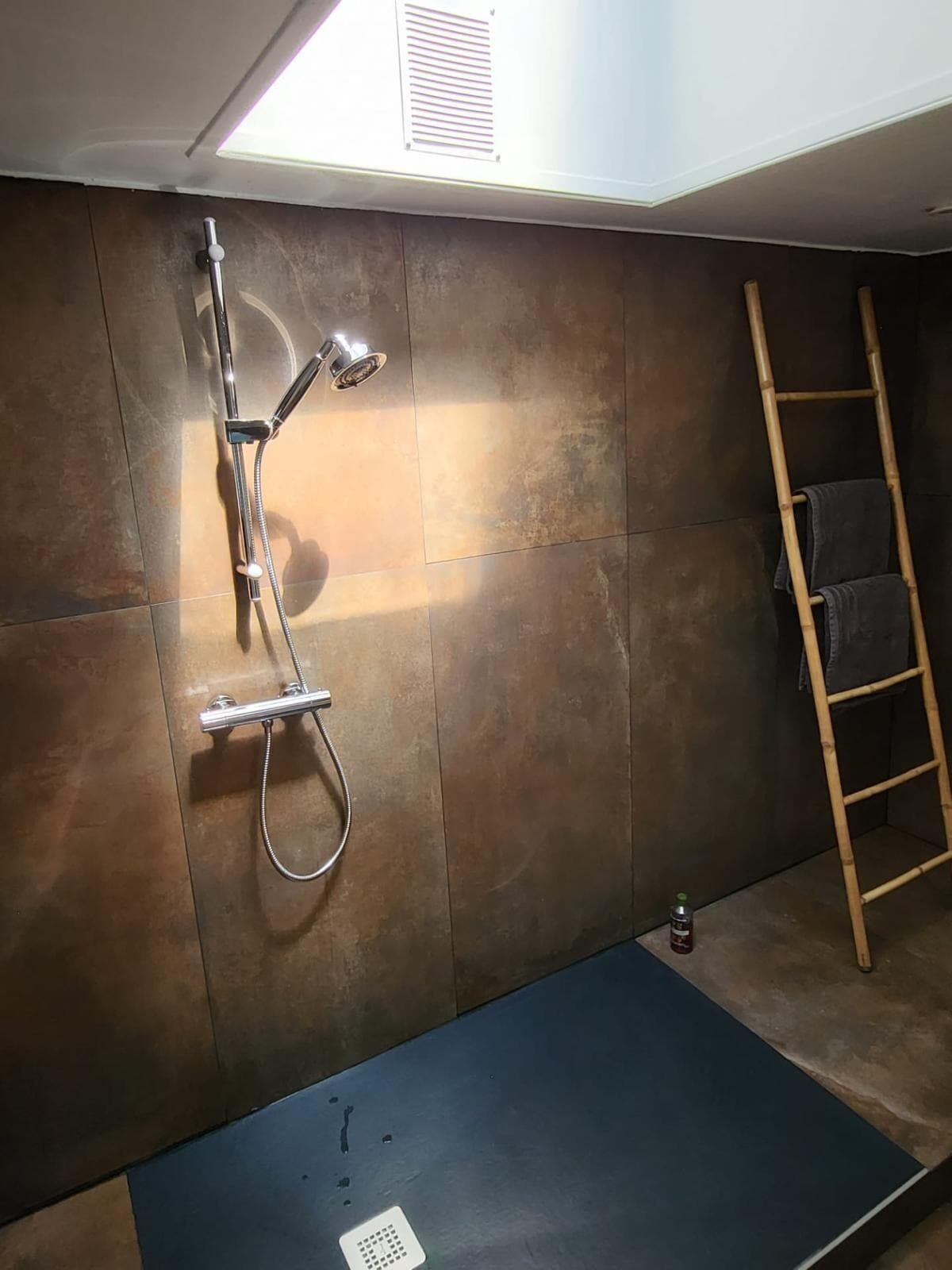 A shower area with a wall-mounted showerhead and a wooden ladder.