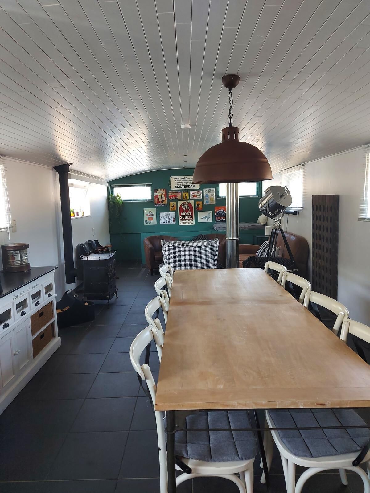 A dining area with a long wooden table, white chairs, and a hanging light fixture.