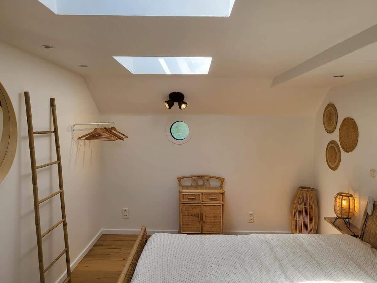 Een slaapkamer met dakraam, een bed, een kledingkast, een ladder en decoratieve muurkunst.