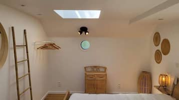 Een slaapkamer met dakraam, een bed, een kledingkast, een ladder en decoratieve muurkunst.