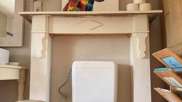 A bathroom with a white toilet, a wooden stool, a mirror, and a colorful giraffe painting above the toilet.