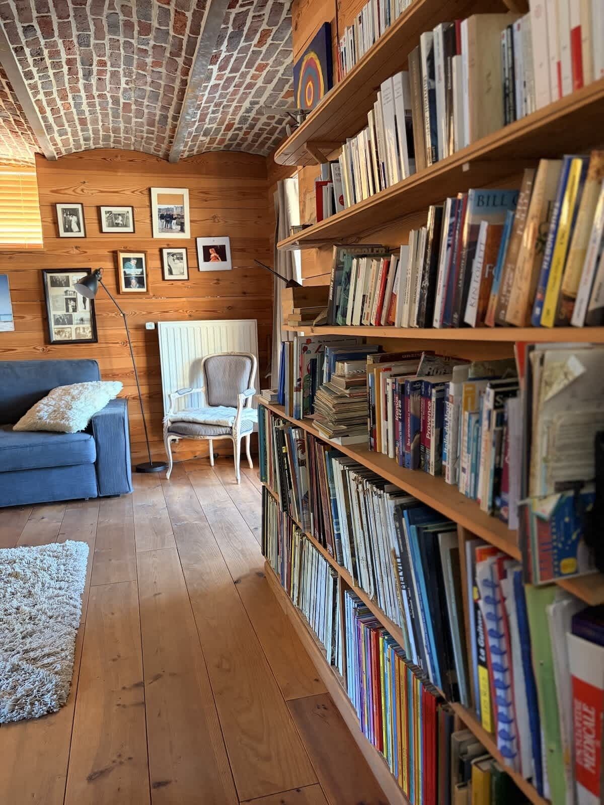 A cozy room with a wooden ceiling, a bookshelf filled with books, a blue sofa, and a chair.