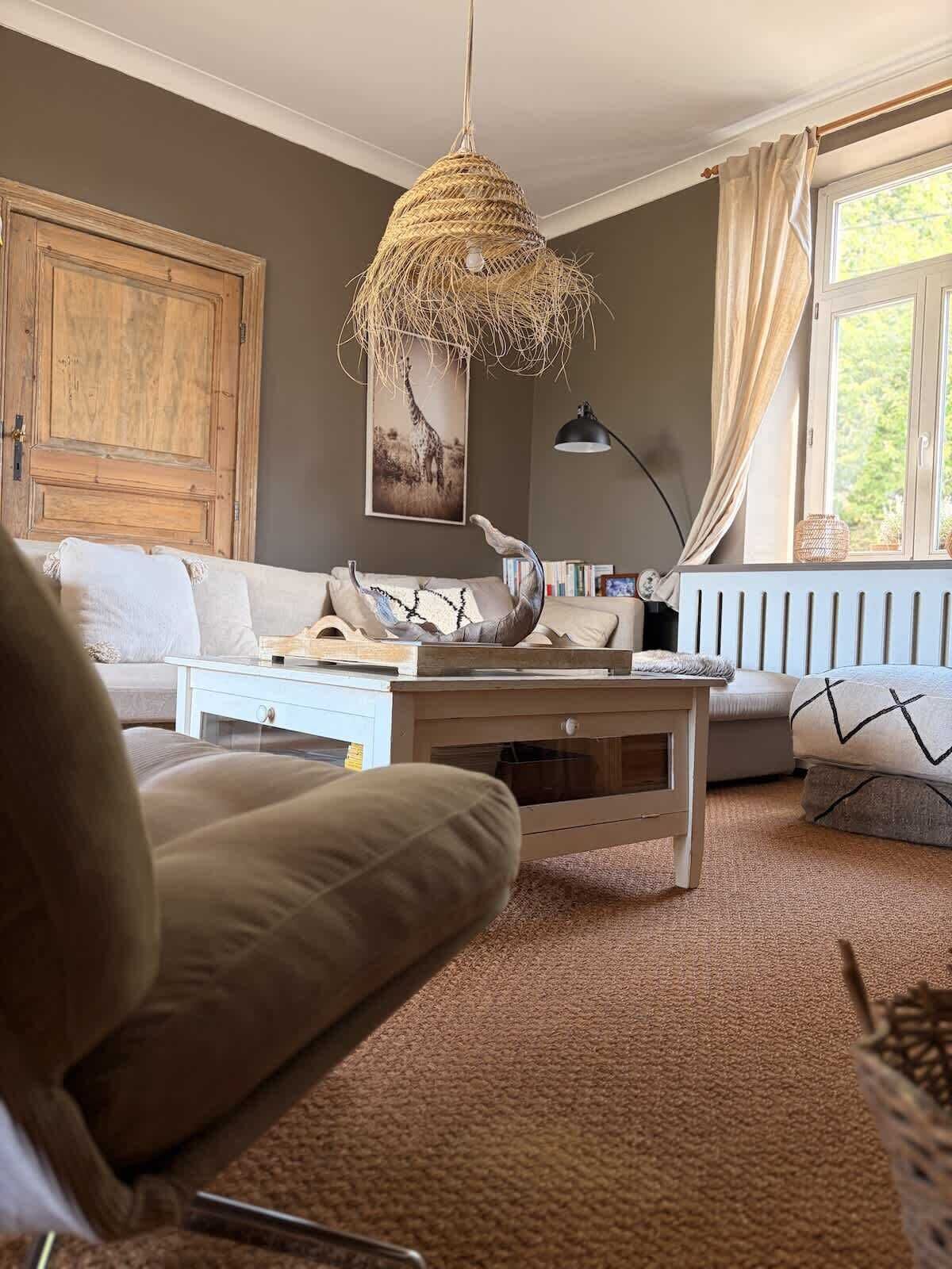 Ein Wohnzimmer mit Sofa, Couchtisch, einer Pendelleuchte, einer Heizung und einem Fenster mit Vorhängen.