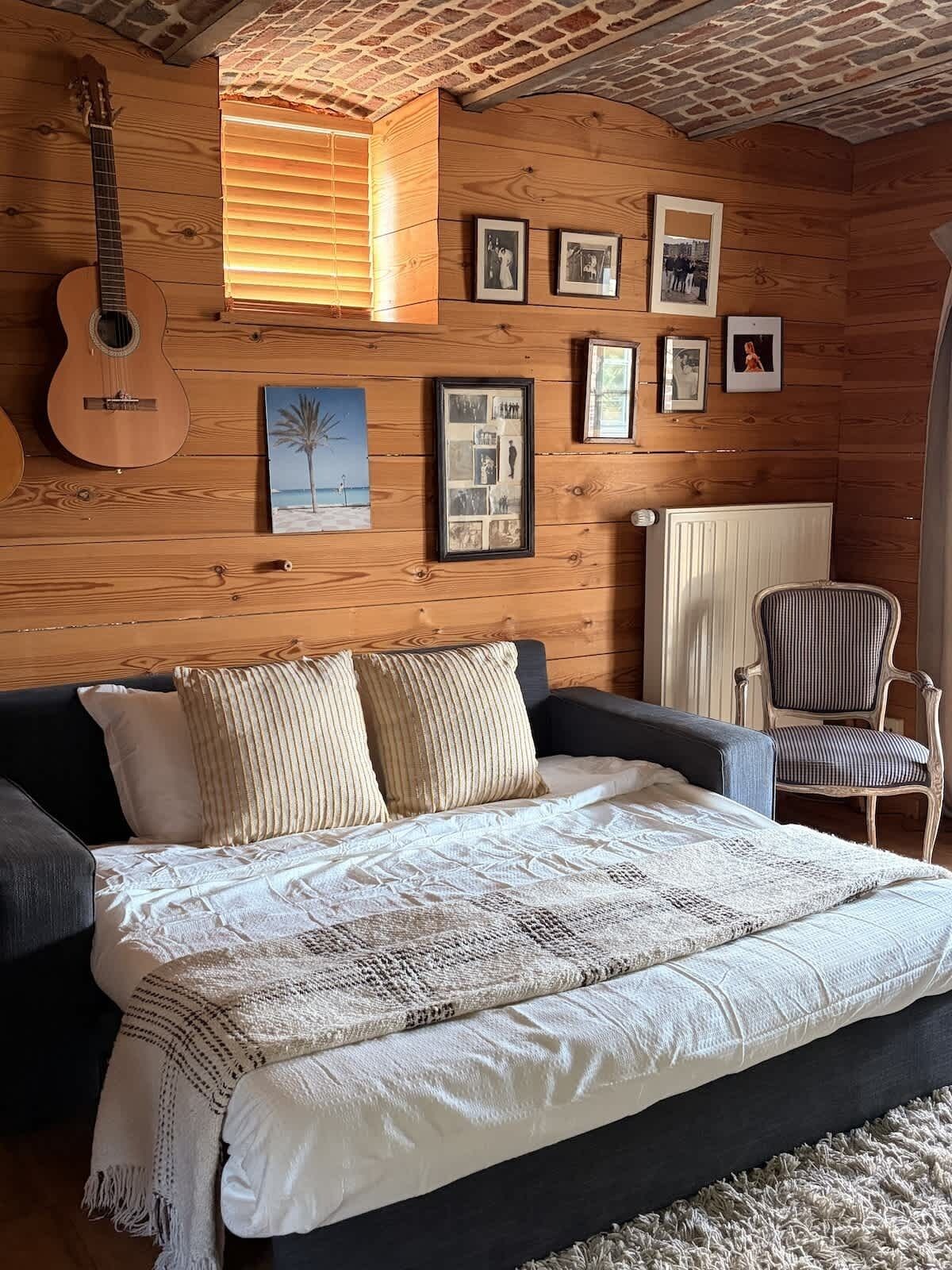 Een knus vertrek met een bed, een gitaar en foto's in lijsten aan de muur.
