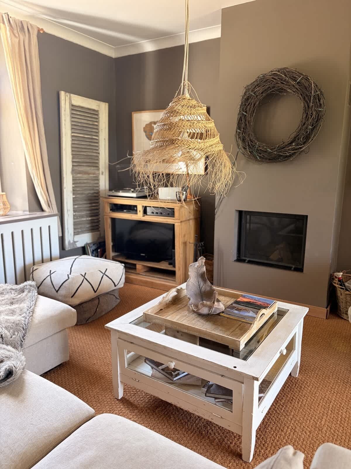 A living room with a white coffee table, a television, a fireplace, and a woven light fixture.