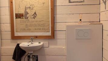 A bathroom with a wooden-framed poster, a sink, a toilet, and a small shelf with a bottle.