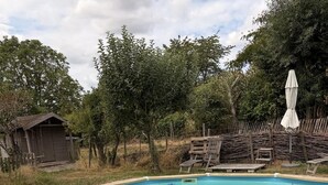 Una piscina con bordo in legno e scaletta metallica, circondata da alberi e una recinzione di legno.