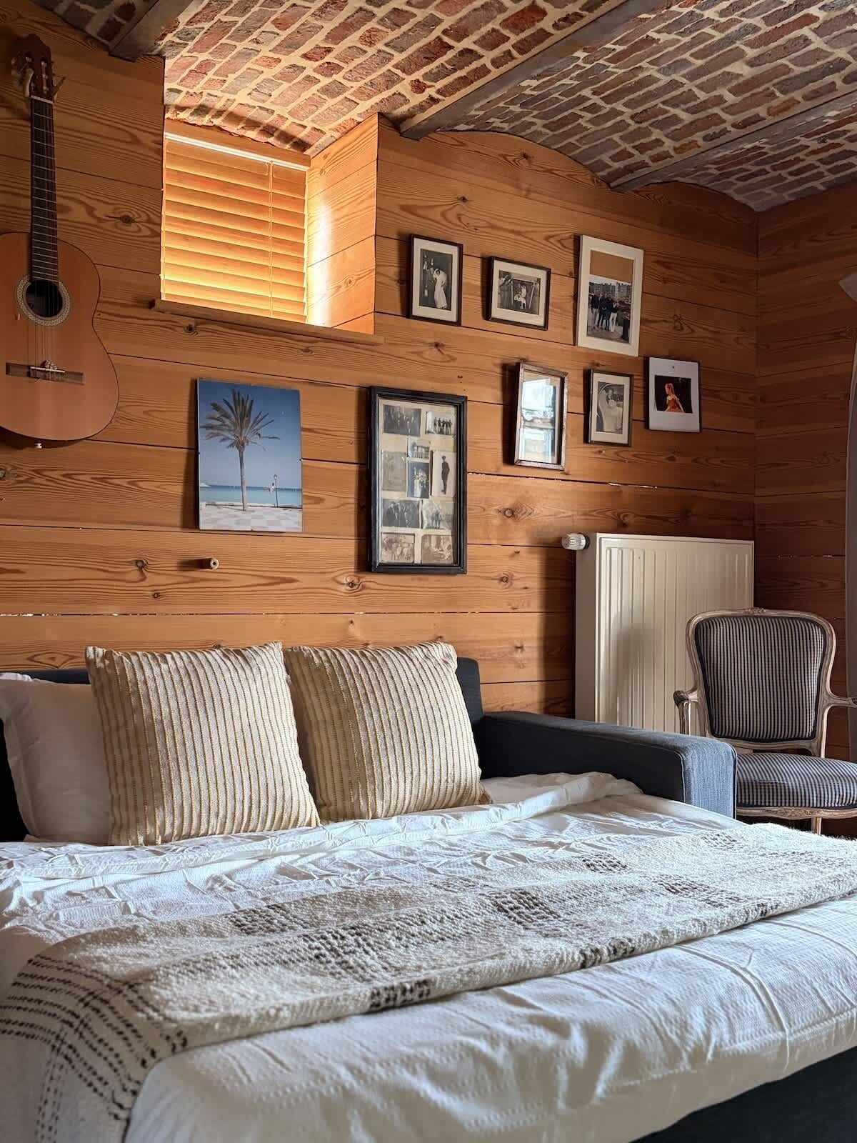 Ein Zimmer mit Holzwänden, einem Bett, einem Sessel und einer Gitarre.