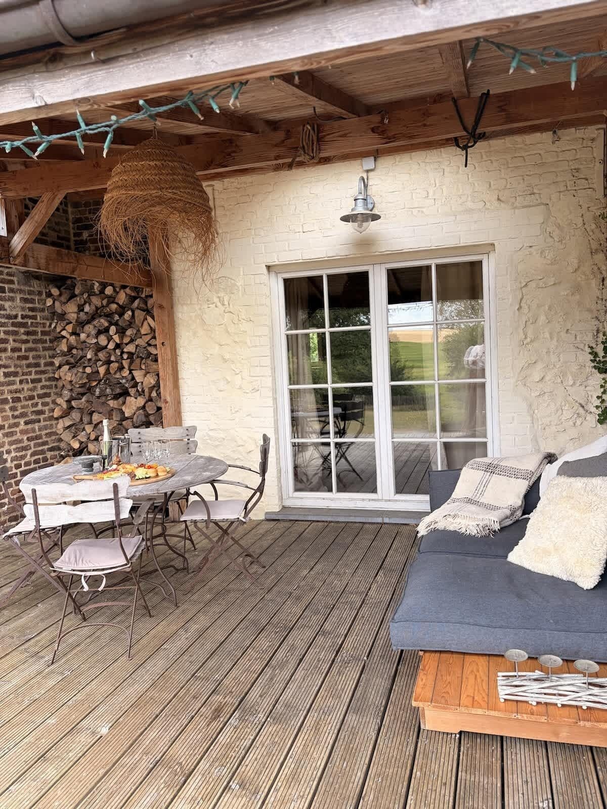 Une terrasse extérieure avec une table et des chaises en bois, un canapé et une grande porte-fenêtre coulissante.