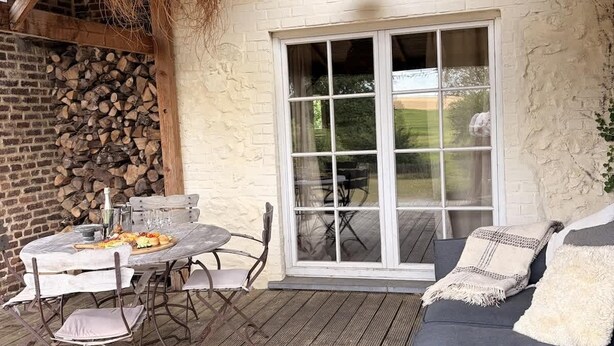 Un patio esterno con tavolo e sedie in legno, un divano e un'ampia porta scorrevole in vetro.