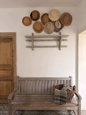 A wooden bench with a woven basket and a wall-mounted hat rack with various hats.