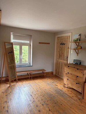 A room with wooden flooring, a bench, a wooden dresser, a door, and a window with a view of greenery. - Charmant cottage à la campagne (Jodoigne)