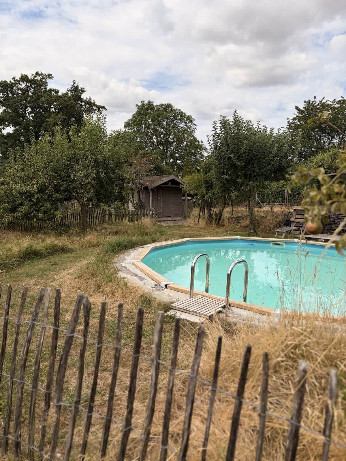 A swimming pool with a wooden deck and metal ladders, surrounded by a wooden fence and trees.