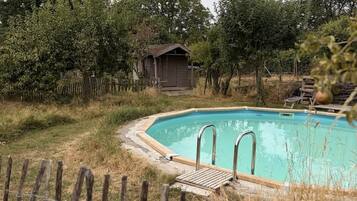 A swimming pool with a wooden deck and metal ladders, surrounded by a wooden fence and trees.