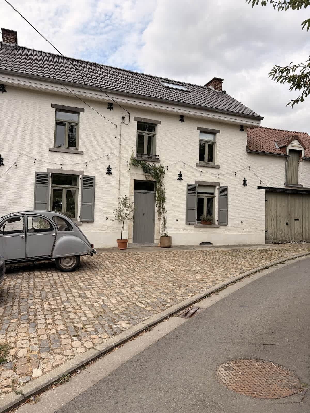 En toetagers bygning med en brostensbelagt indkørsel og en parkeret veteranbil.