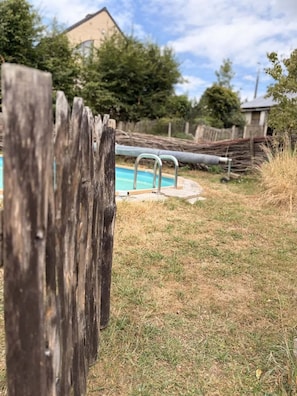 A wooden fence in the foreground with a swimming pool in the background.