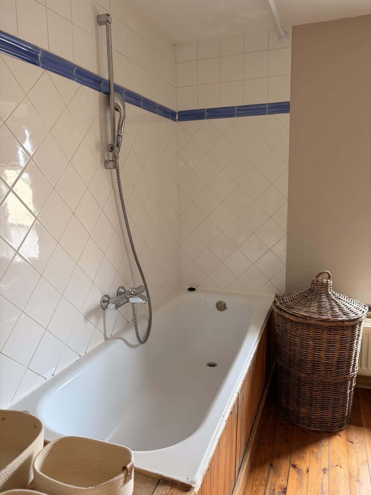 A bathroom with a white bathtub, a shower, and a wicker basket.