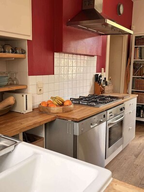 A kitchen with a gas stove, oven, and a wooden countertop with a fruit bowl. - Charmant cottage à la campagne (Jodoigne)
