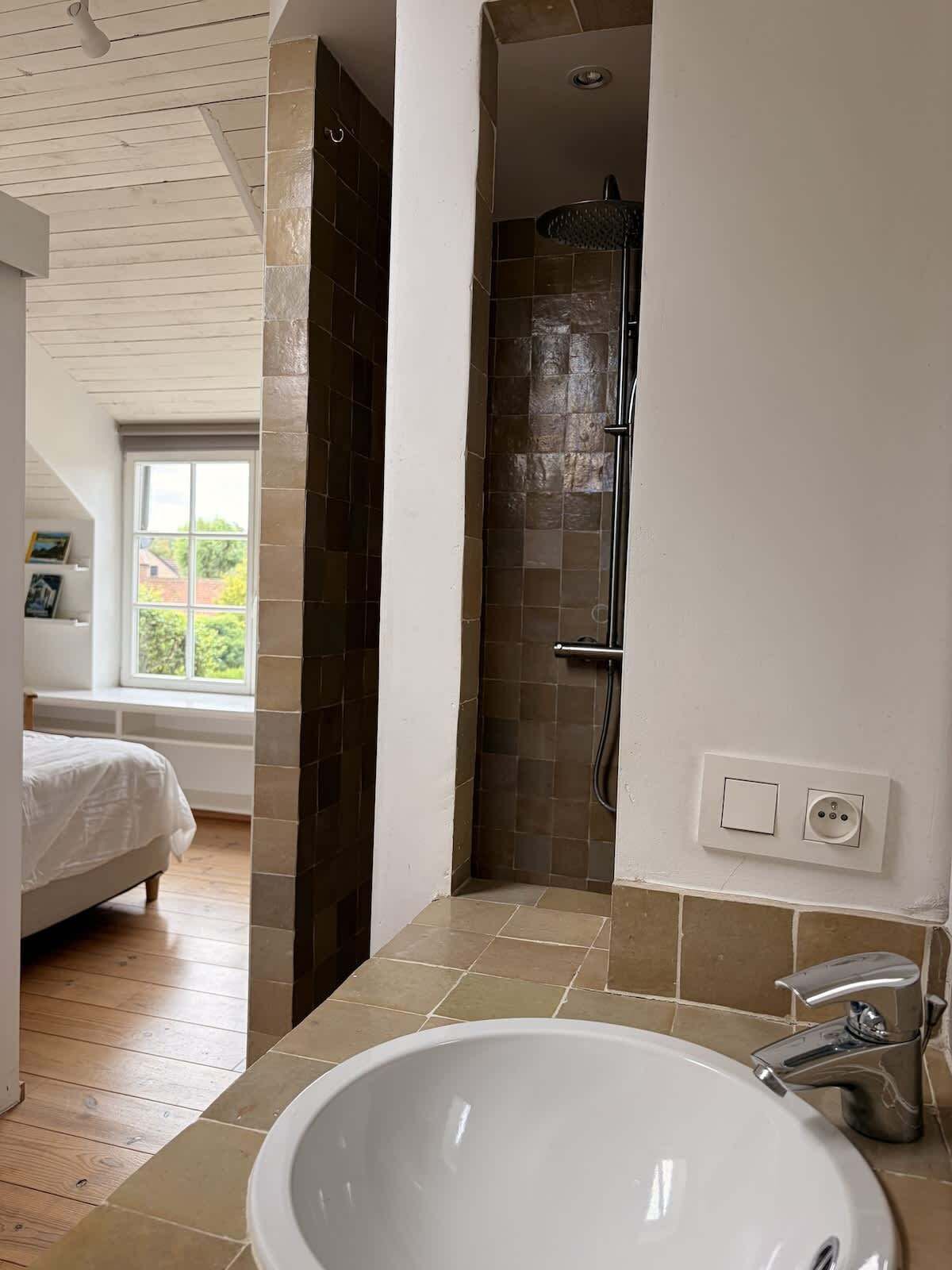 A bathroom with a shower, a sink, and a window.
