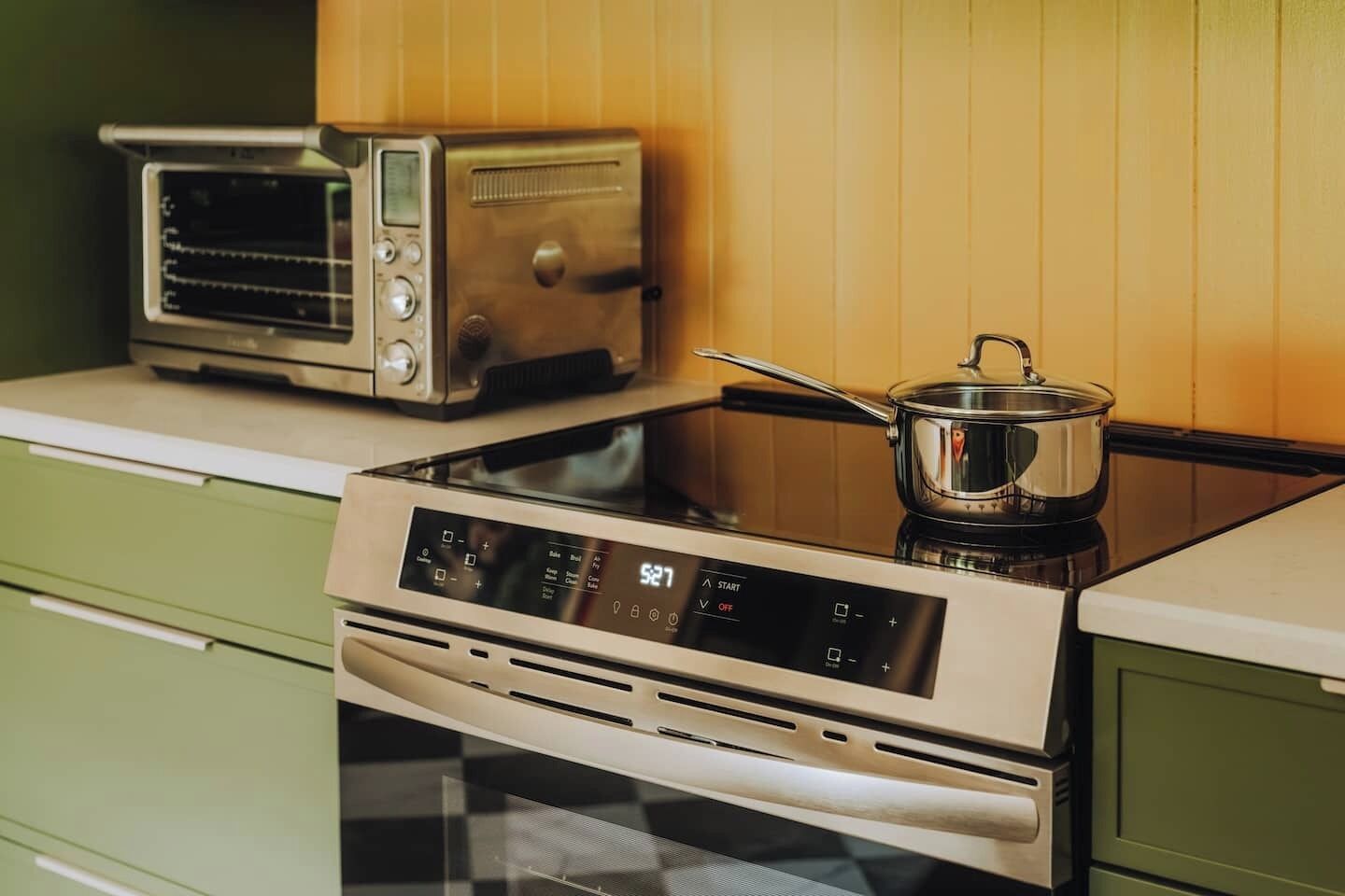 A kitchen with a stove, a toaster, and a pot on the counter.