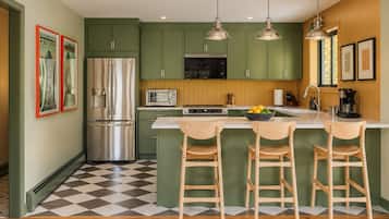 Una cocina con armarios verdes, un refrigerador de acero inoxidable, un microondas y un fregadero con taburetes de bar.