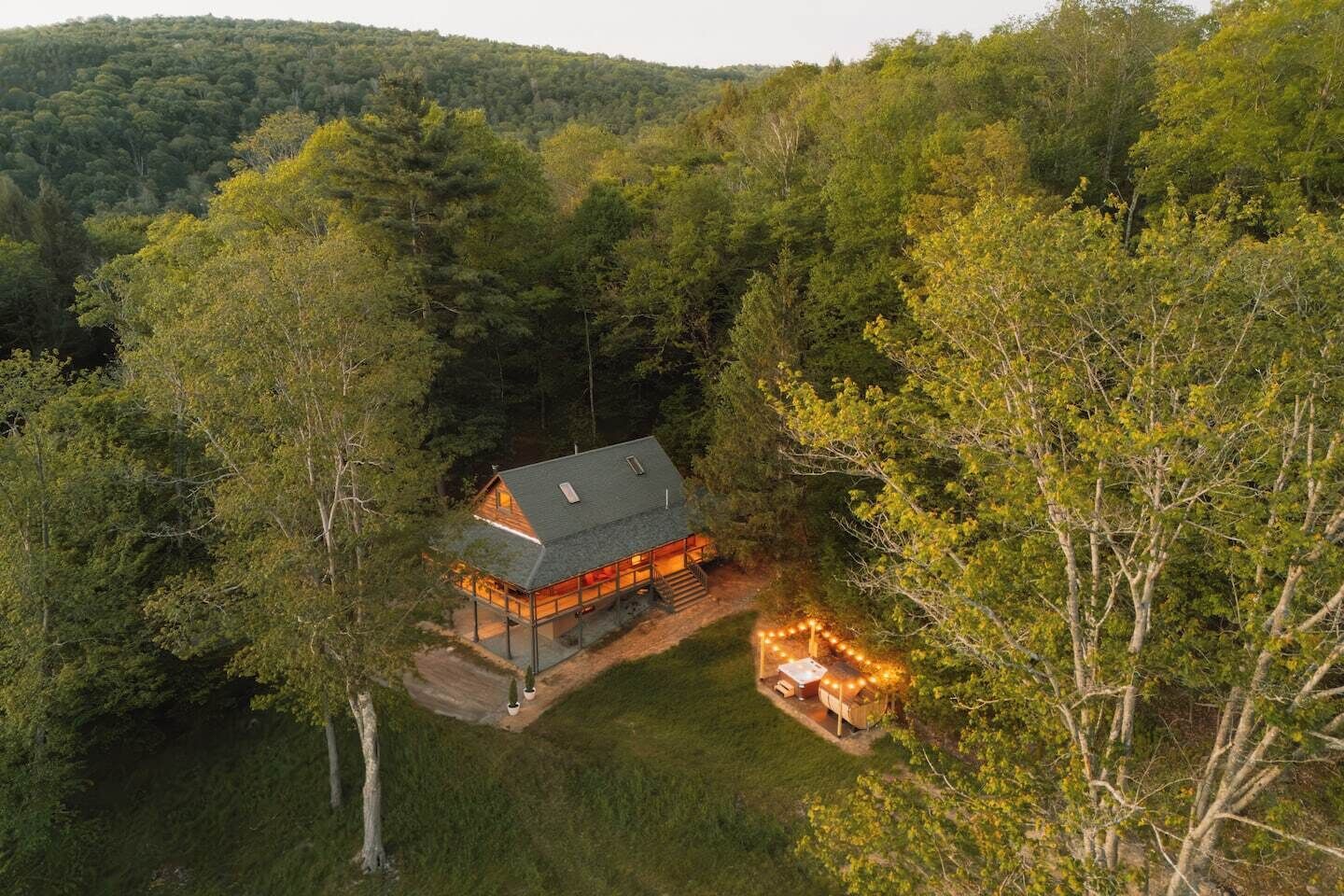 A cabin surrounded by dense forest, with a visible deck and outdoor lighting.