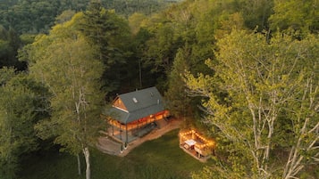 A cabin surrounded by dense forest, with a visible deck and outdoor lighting.