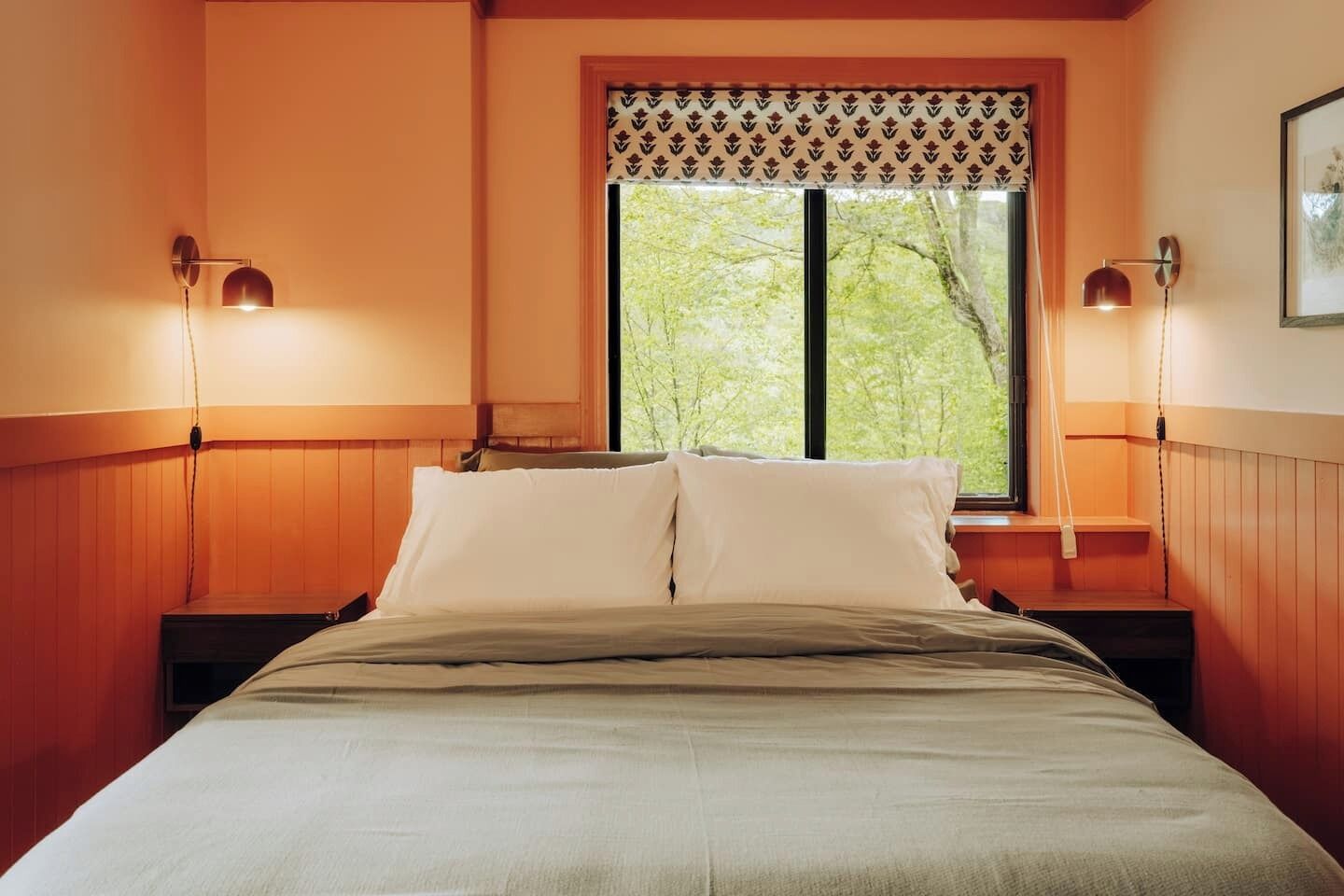 A bed with a headboard, two bedside lamps, and a window with a patterned blind.