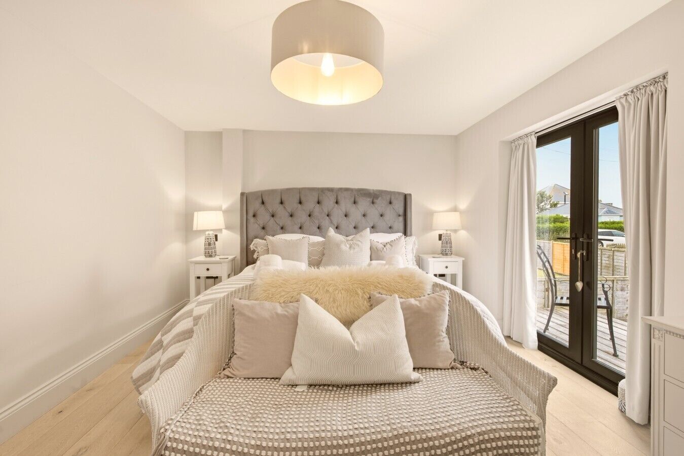 Een slaapkamer met een groot bed, twee nachtkastjes, een kroonluchter en uitzicht door een schuifdeur.