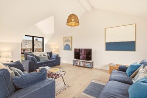 Un salon moderne avec un plafond haut, un téléviseur et une bibliothèque.