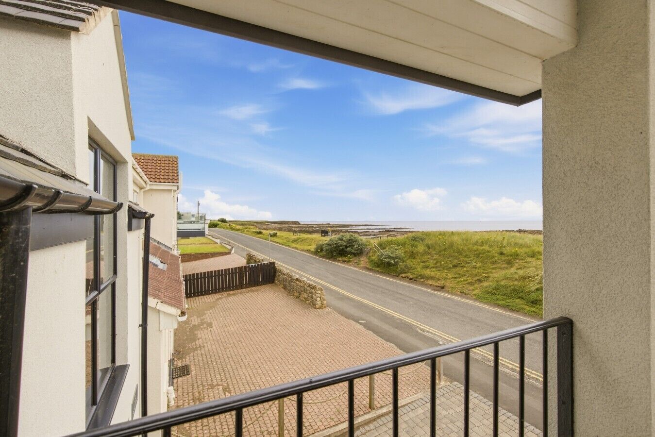 Una proprietà residenziale con vialetto lastricato che conduce a una strada, vista sul mare e cielo sereno.