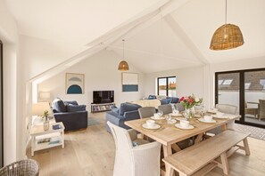 A spacious living area with a high ceiling, a dining table set for four, and a comfortable seating arrangement. - Seaside House - North East Escapes (Beadnell)