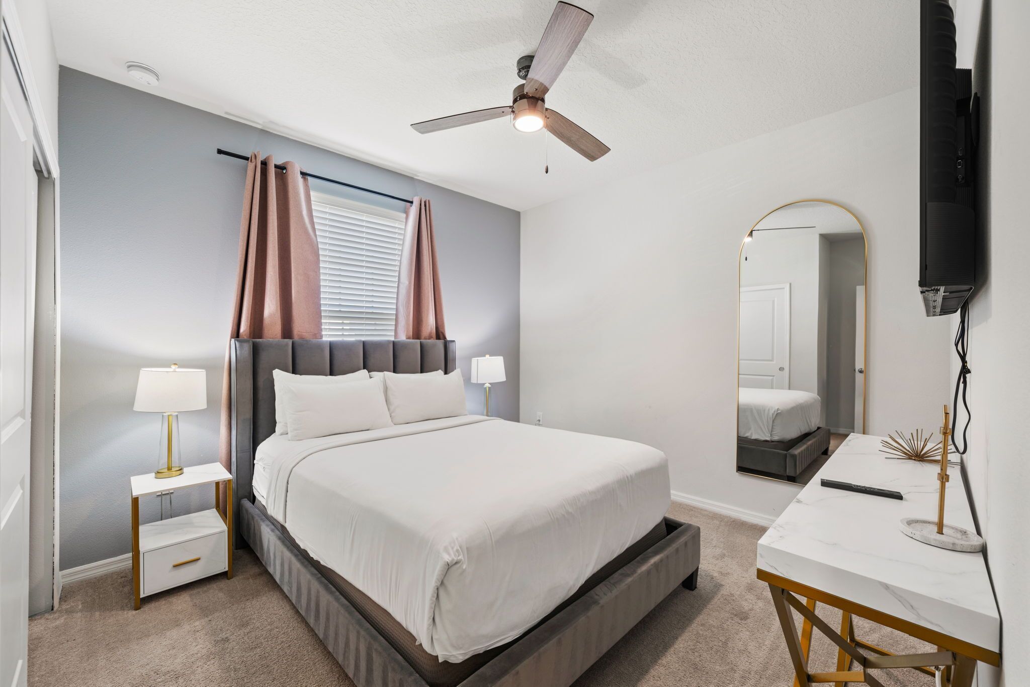 A bedroom with a bed, bedside tables, a ceiling fan, a mirror, and a TV.