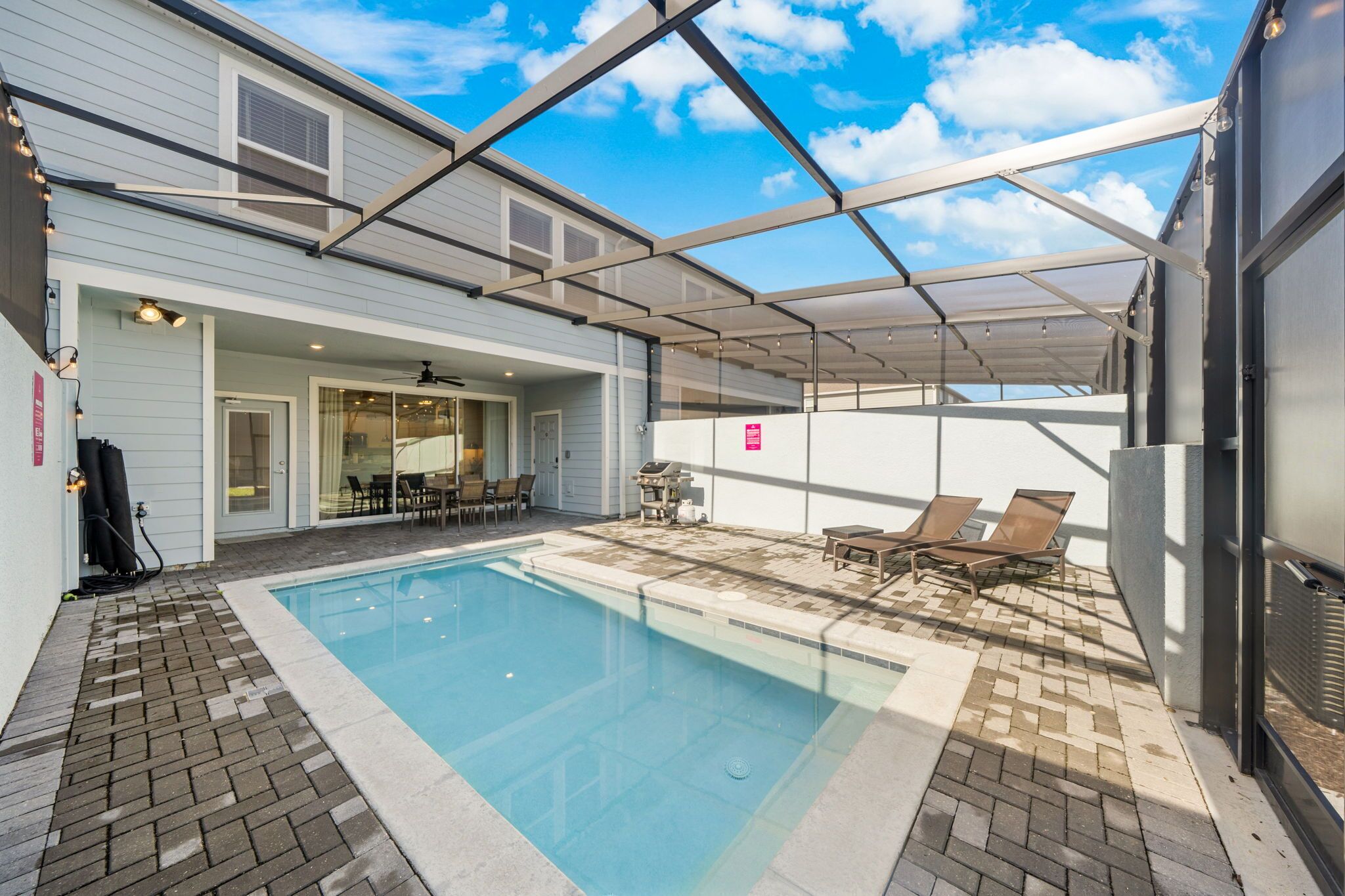 A swimming pool with a covered patio area, outdoor seating, and a grill.